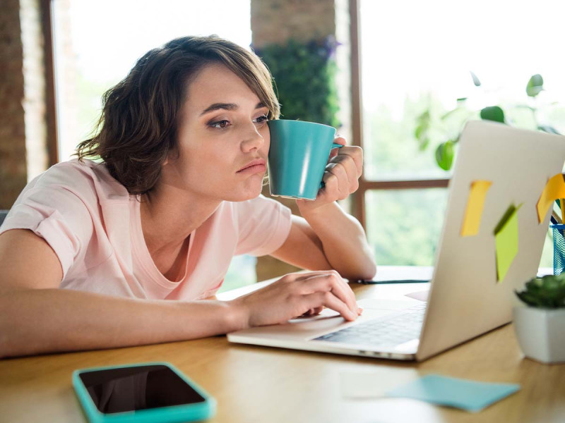 Eine Mitarbeiterin sitzt gelangweilt an ihrem Arbeitsplatz, was typische Symptome eines Boreout zeigt. Sie ist im Job unterfordert, da die Unterforderung im Job das Gegenteil von Burnout darstellt. Die Unterforderung am Arbeitsplatz ist offensichtlich, da sie sich nicht gefordert fühlt.