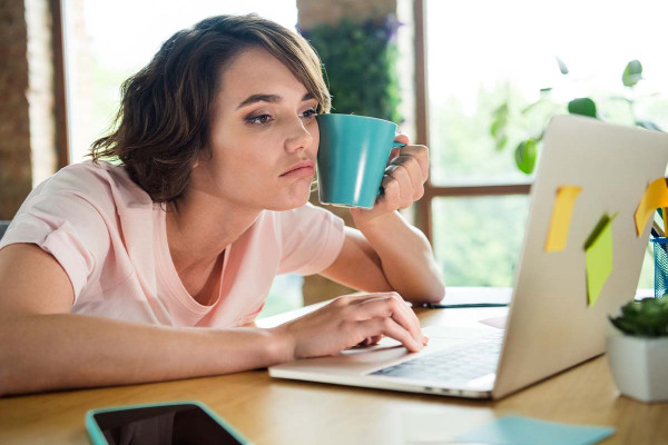 Eine Mitarbeiterin sitzt gelangweilt an ihrem Arbeitsplatz, was typische Symptome eines Boreout zeigt. Sie ist im Job unterfordert, da die Unterforderung im Job das Gegenteil von Burnout darstellt. Die Unterforderung am Arbeitsplatz ist offensichtlich, da sie sich nicht gefordert fühlt.