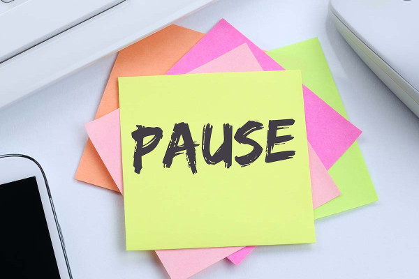 Post-it-Zettel mit der Aufschrift 'Pause' auf einem Schreibtisch, umgeben von Arbeitsutensilien wie Tastatur und Smartphone – symbolisiert gesetzlich vorgeschriebene Pausenzeiten und Erholung im Arbeitsalltag.