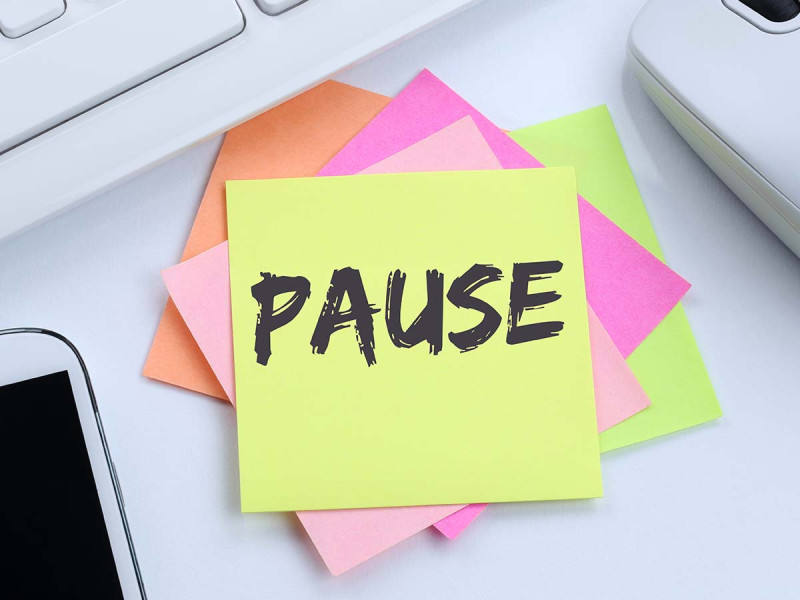 Post-it-Zettel mit der Aufschrift 'Pause' auf einem Schreibtisch, umgeben von Arbeitsutensilien wie Tastatur und Smartphone – symbolisiert gesetzlich vorgeschriebene Pausenzeiten und Erholung im Arbeitsalltag.