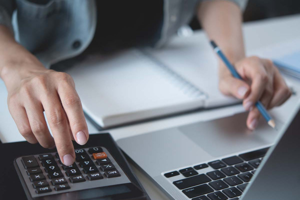 Person berechnet Steuern und Buchhaltung am Laptop mit Taschenrechner, erstellt Lohnabrechnung für nebenberuflich selbstständige Kleinunternehmer und Freelancer.